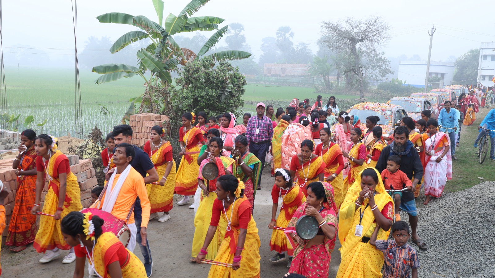 Women in yellow saris leading a village procession with drums